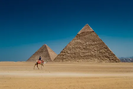 A man rides a camel in view of the remarkable Egyptian pyramids.