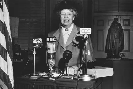Eleanor Roosevelt standing in front of four microphones labeled as CBS and NBC