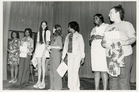 Candid photo of seven women holding papers standing in a line on stage.