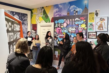eople stand near a mural by the artist Cita Sadeli, and listen to her talking about why and how she made the mural.