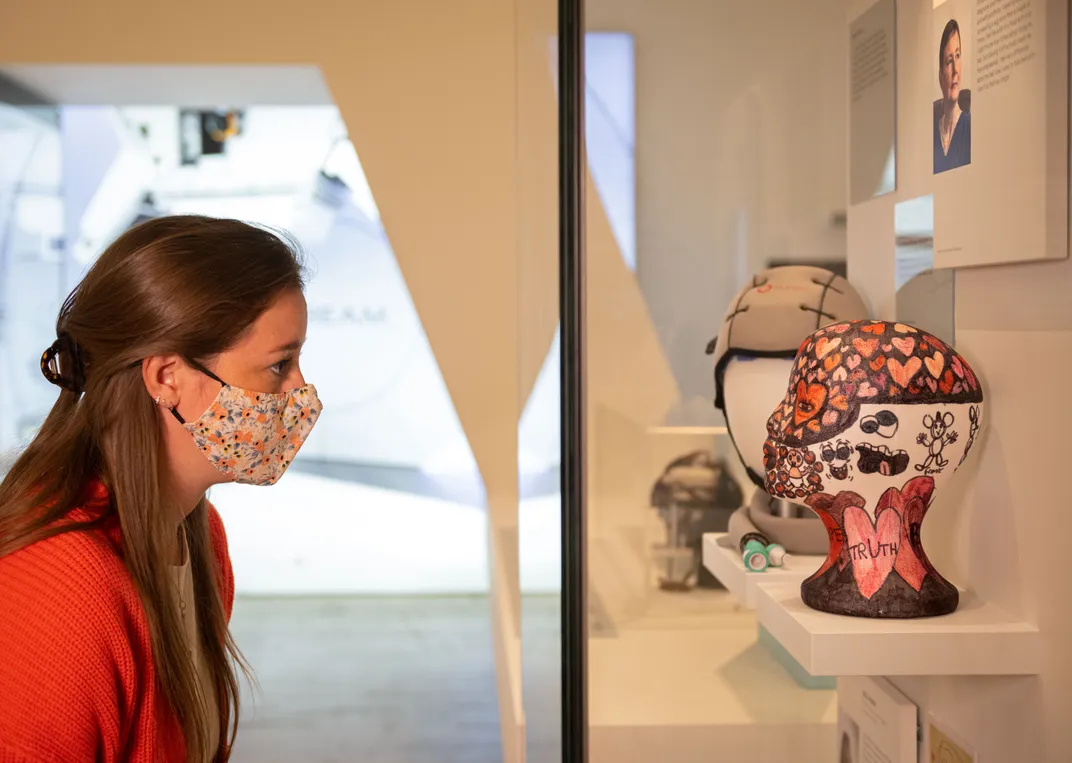 Visitor in Cancer Revolution at the Science Museum looking at cancer patient Sarah's wig stand decorated by her daughter.