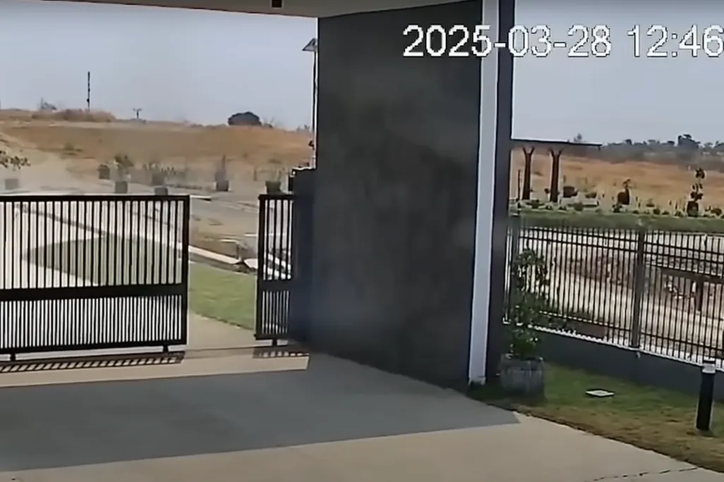 screenshot of cctv footage shows a gate in the foreground and electrical infrastructure and a cloud of dirt in the background